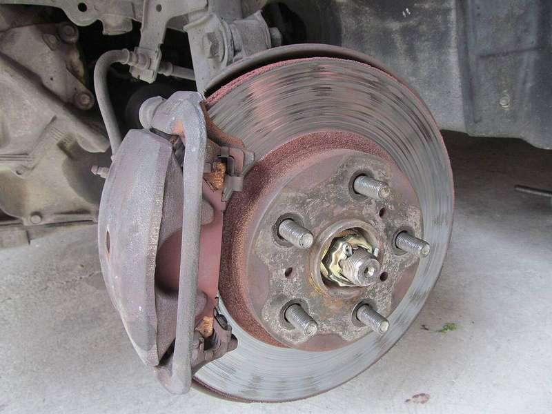 A worn car disc brake with surface rust on the rotor