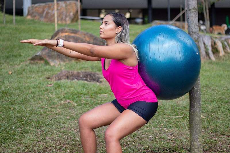 Squats performed against a stability ball, a supported way to practice depth while ankle mobility improves.