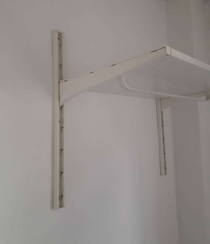 A white adjustable metal shelf bracket, whose length creates leverage on its wall anchors