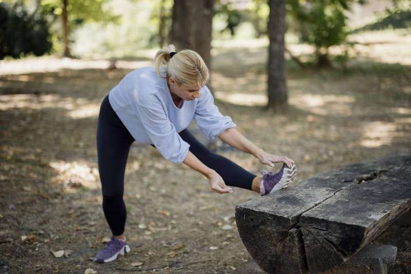 A woman stretches her leg against a park bench, showing the calf-stretching habit recommended before bed