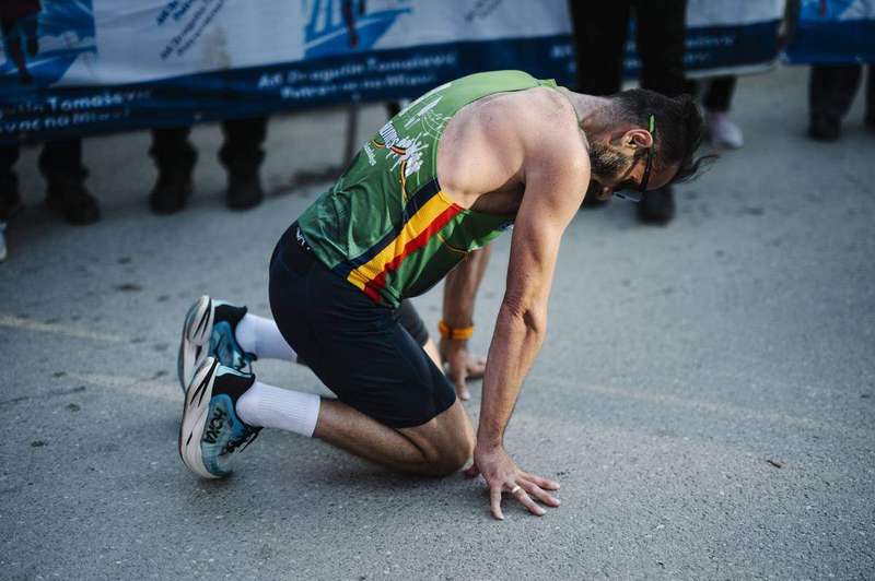 A runner kneeling on the street after finishing a marathon