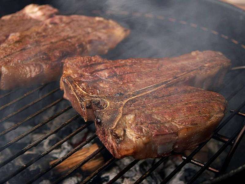 Porterhouse steaks grilling over an open flame