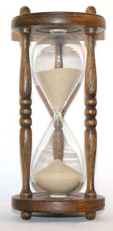 A wooden hourglass, its upper bulb emptying as the minutes pass