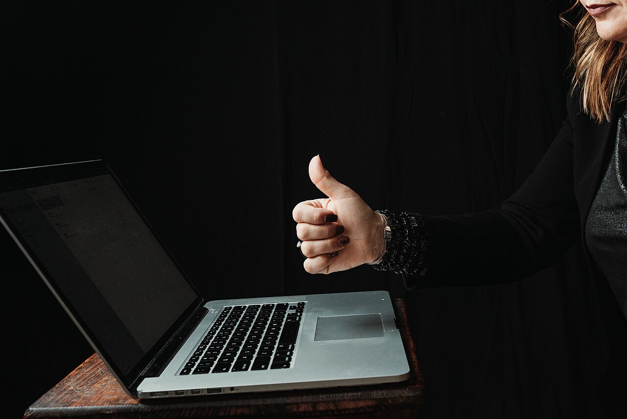 A freelancer giving a thumbs up while working on a laptop at a home office desk