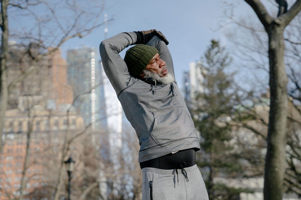 An older man stretching outdoors in a park on a bright day
