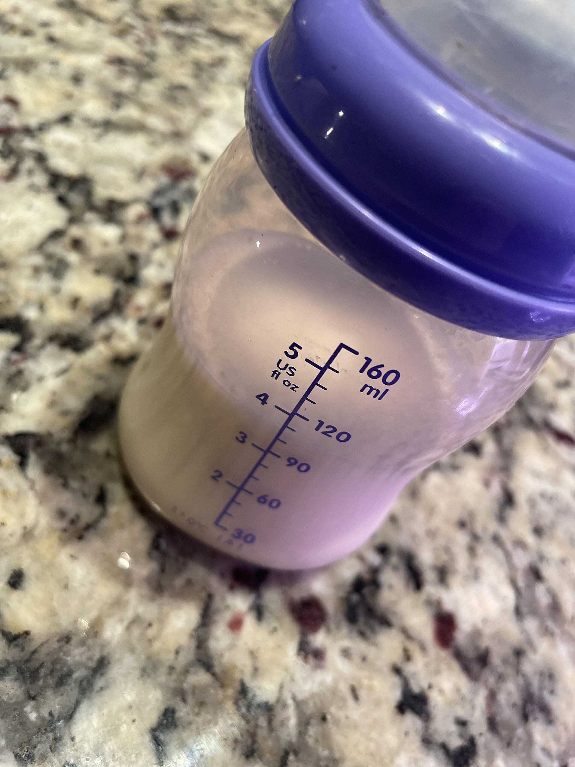 A baby feeding bottle on a table next to an infant