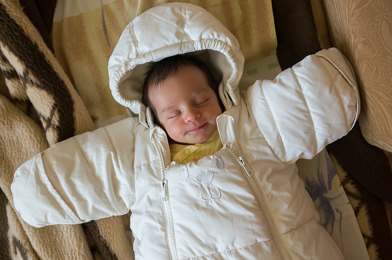 A smiling baby in warm clothes, a reminder of how small and sleepy newborns really are