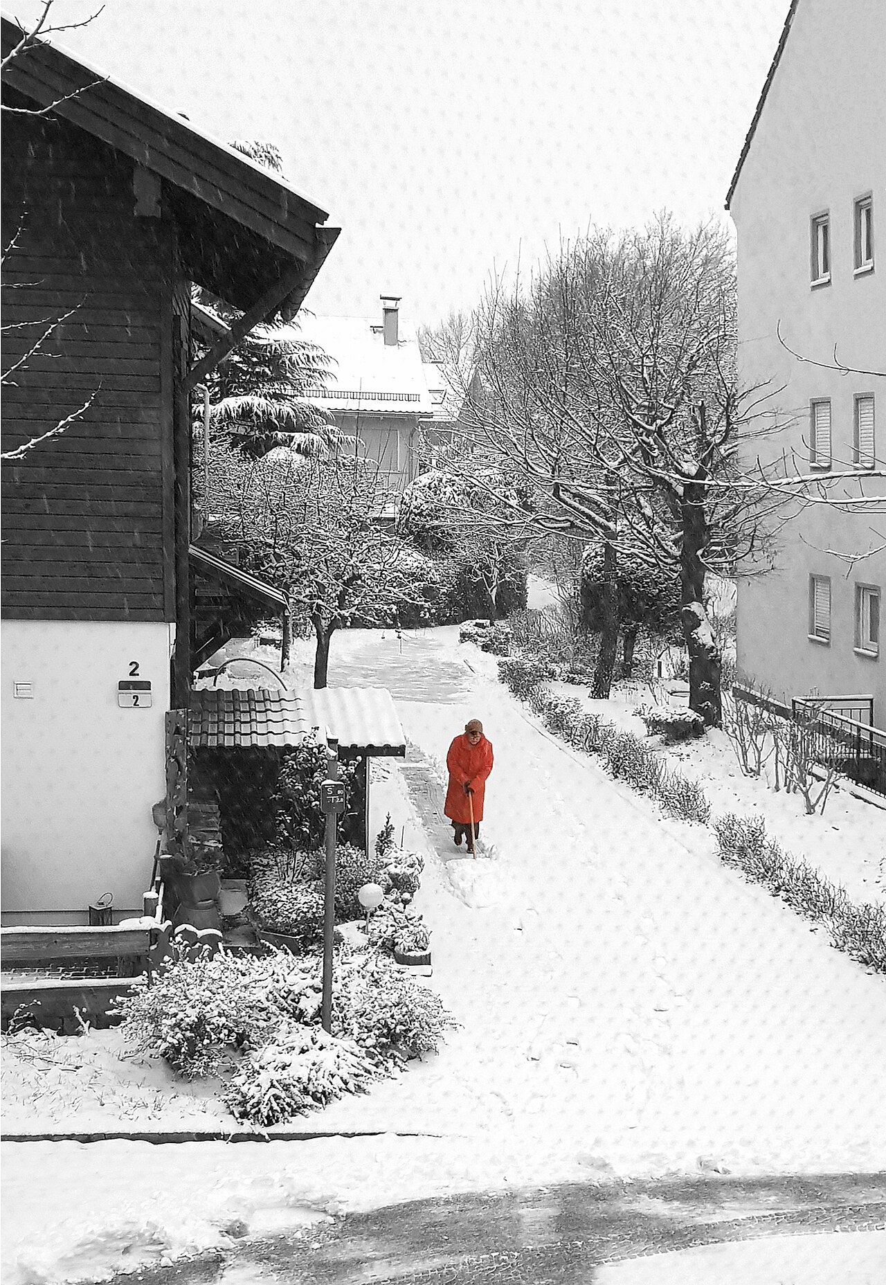 A homeowner clearing snow from a path in front of a house in winter