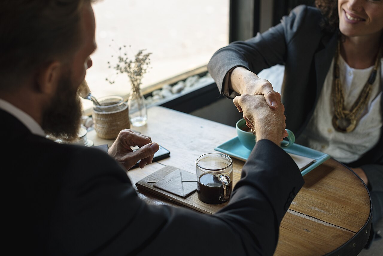 Two people shaking hands over a coffee table in agreement