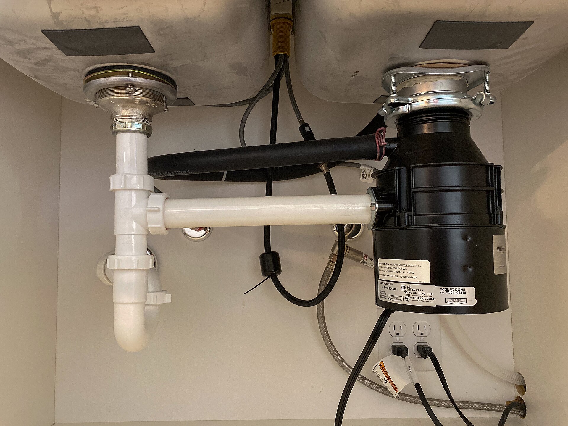 The underside of a garbage disposal unit under a kitchen sink