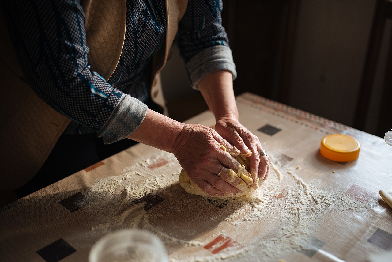 Hands pressing and folding a ball of bread dough on a floured work surface