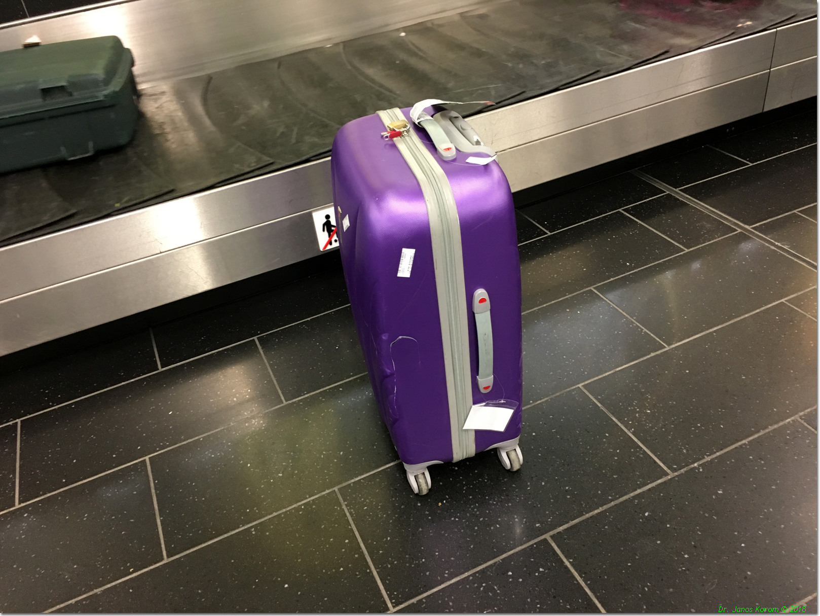 A purple checked suitcase standing beside a baggage carousel