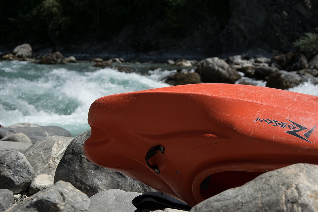 An orange whitewater kayak hull resting on river rocks
