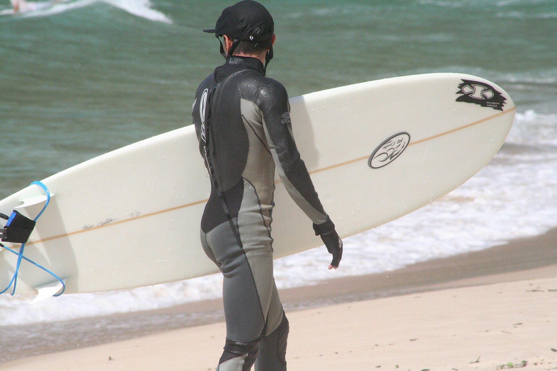 A surfer in a full wetsuit carrying a surfboard on the beach