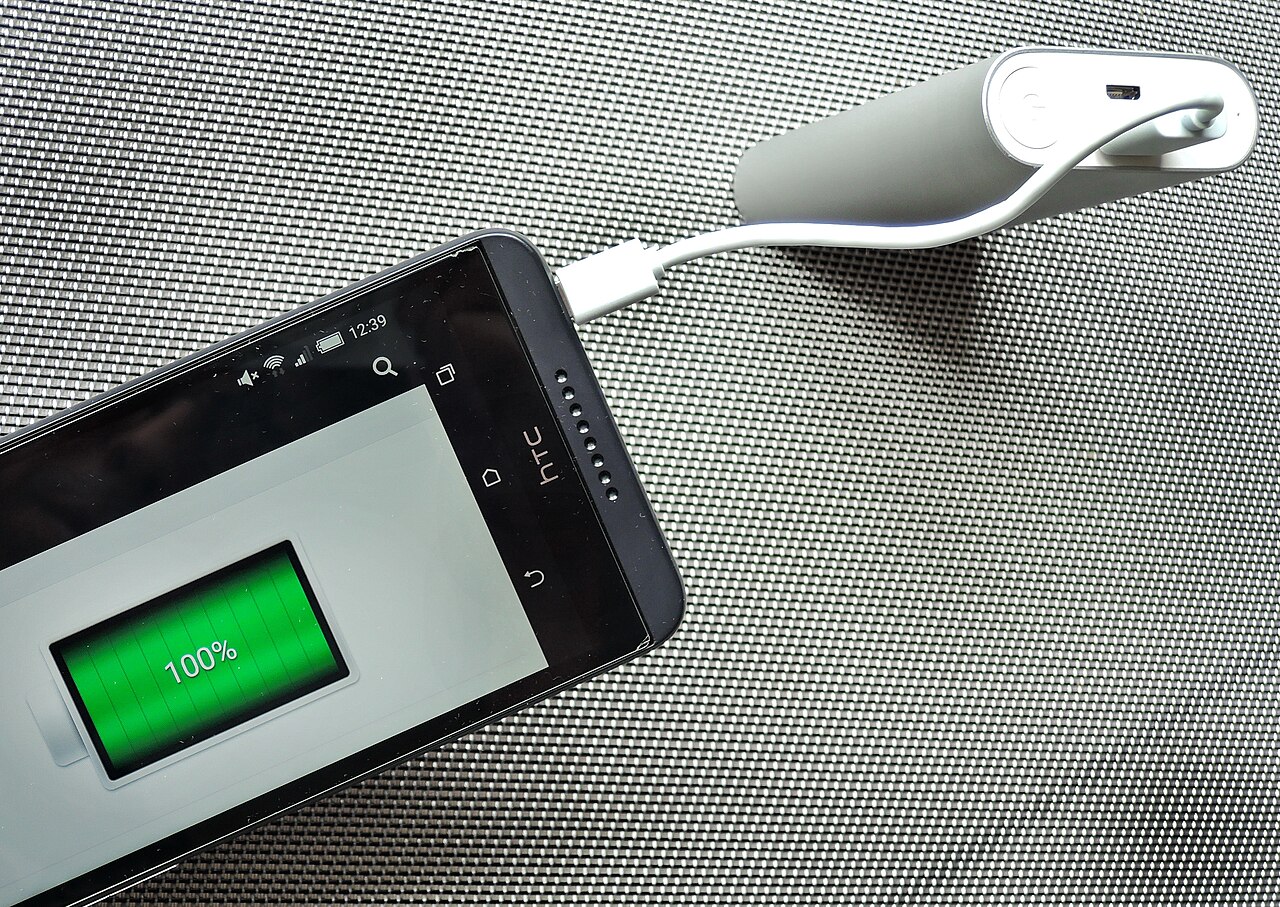 A smartphone charging from a USB power bank on a desk