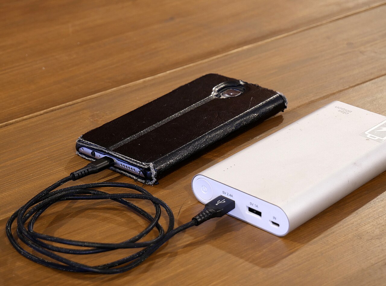 A smartphone charging with a power bank, showing the cable connection