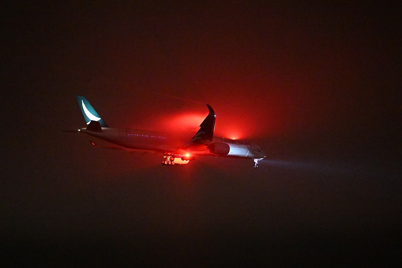 An airliner taxiing in dense fog at night, barely visible beyond its lights