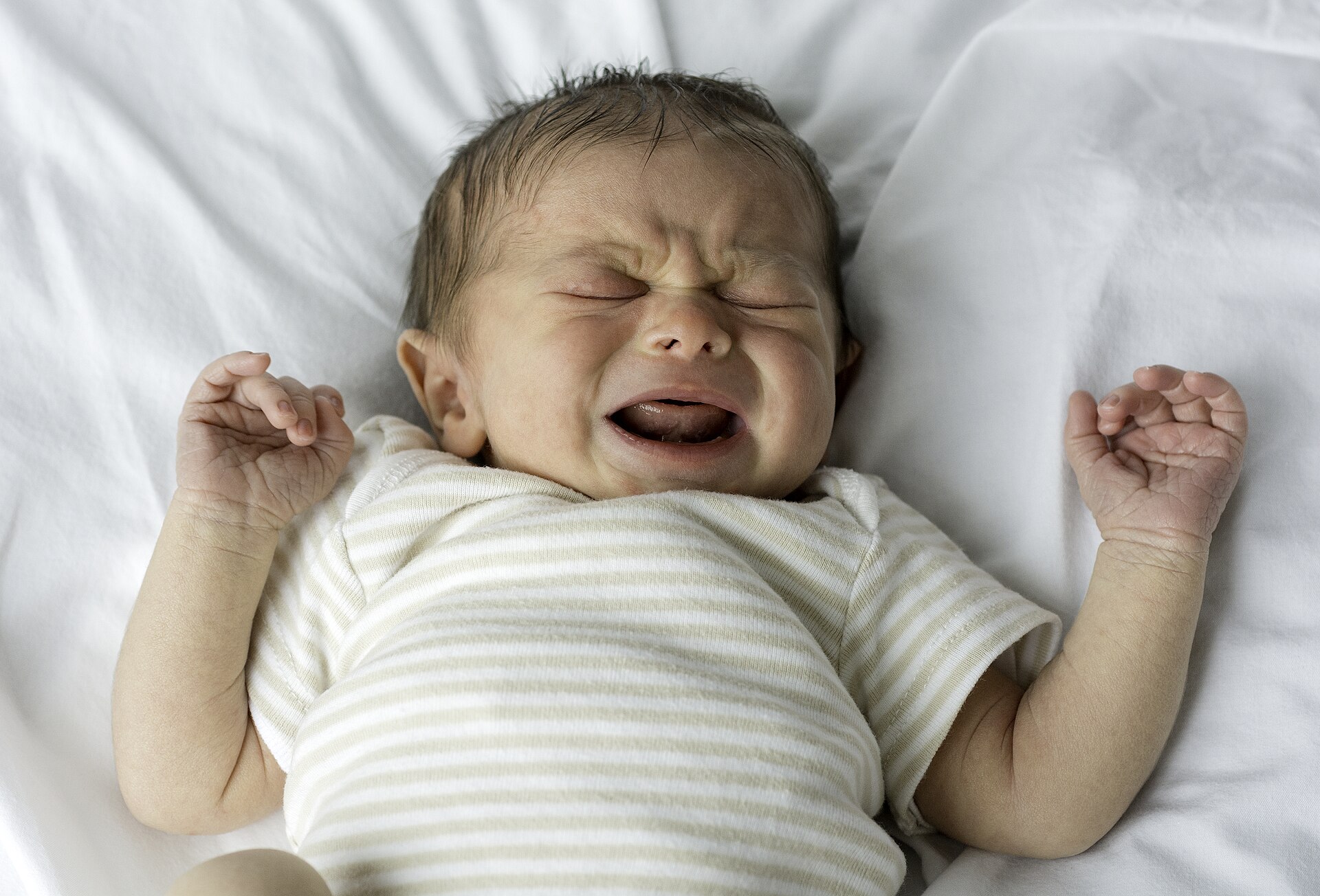 A newborn baby crying with eyes squeezed shut and mouth open