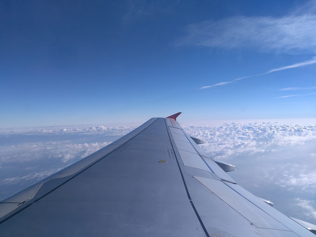 An airplane wing over bright clouds in clear daylight