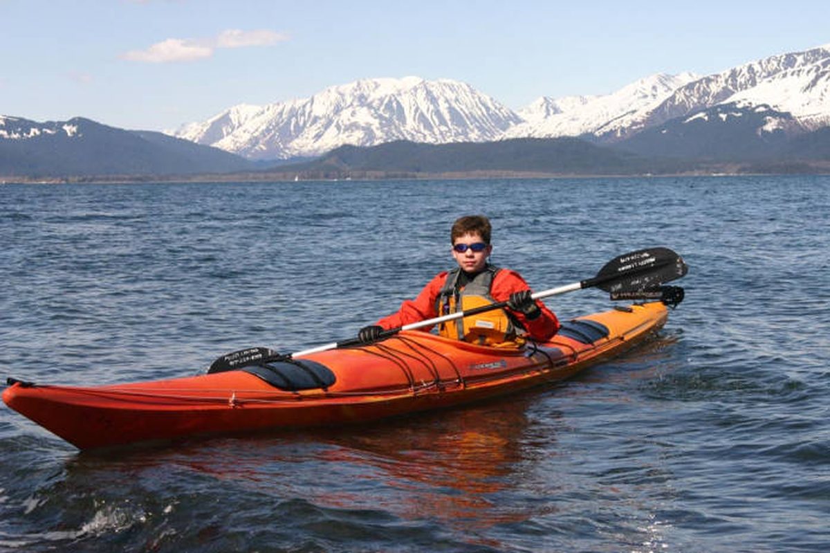 A boy paddling a kayak on calm water