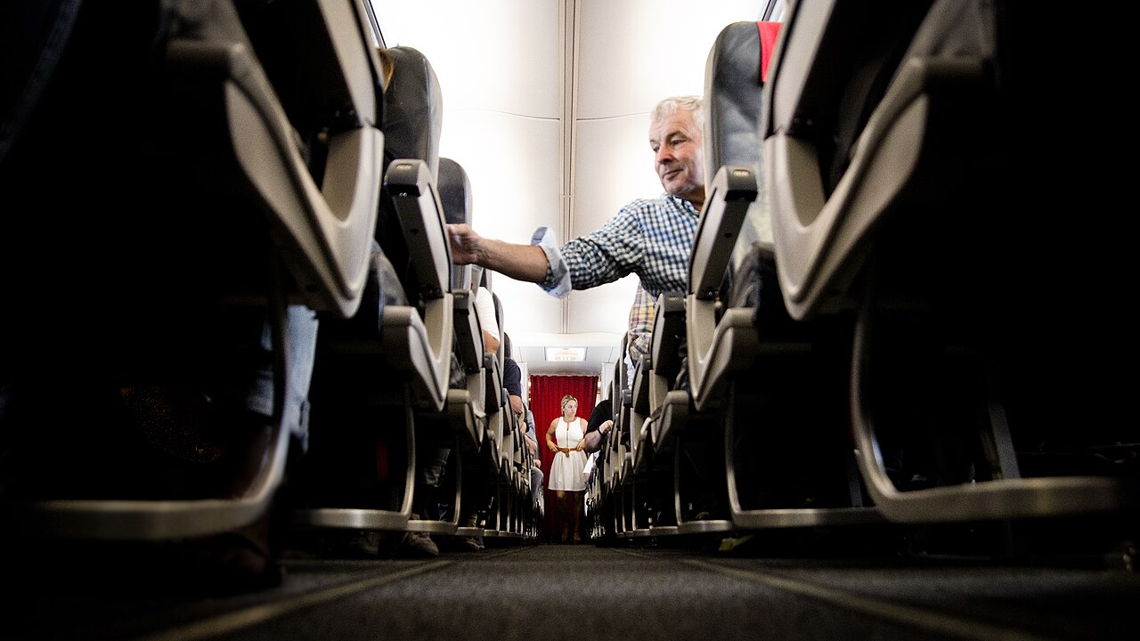 Passengers settling into seats along an airplane cabin aisle