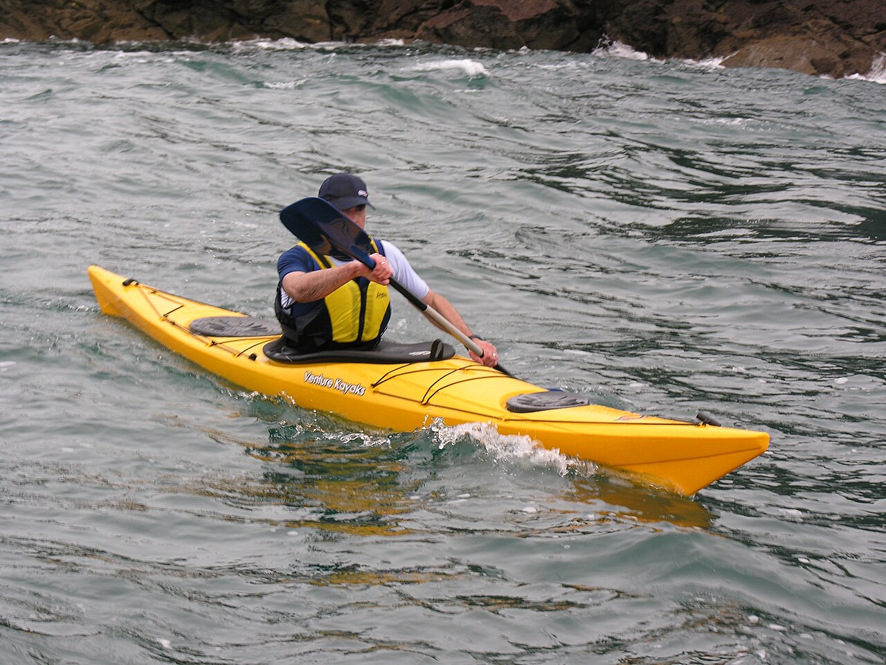 A sea kayaker with a touring paddle on open water