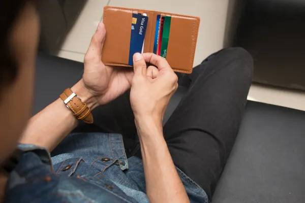 A person holding open a brown leather wallet full of cards