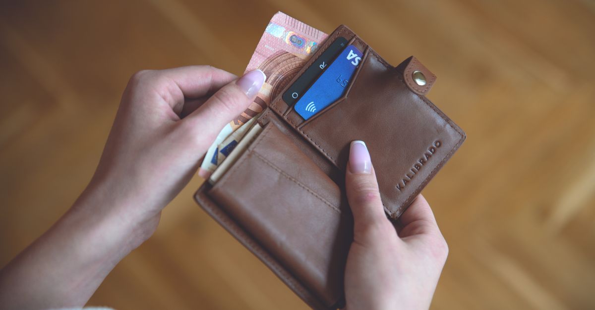 Hands holding a wallet with cash bills and a contactless Visa card
