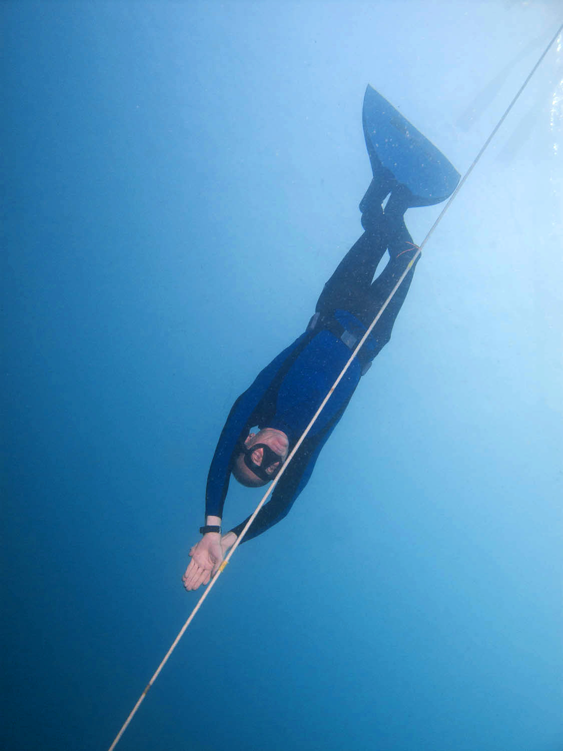 A freediver in clear blue water wearing long freediving fins
