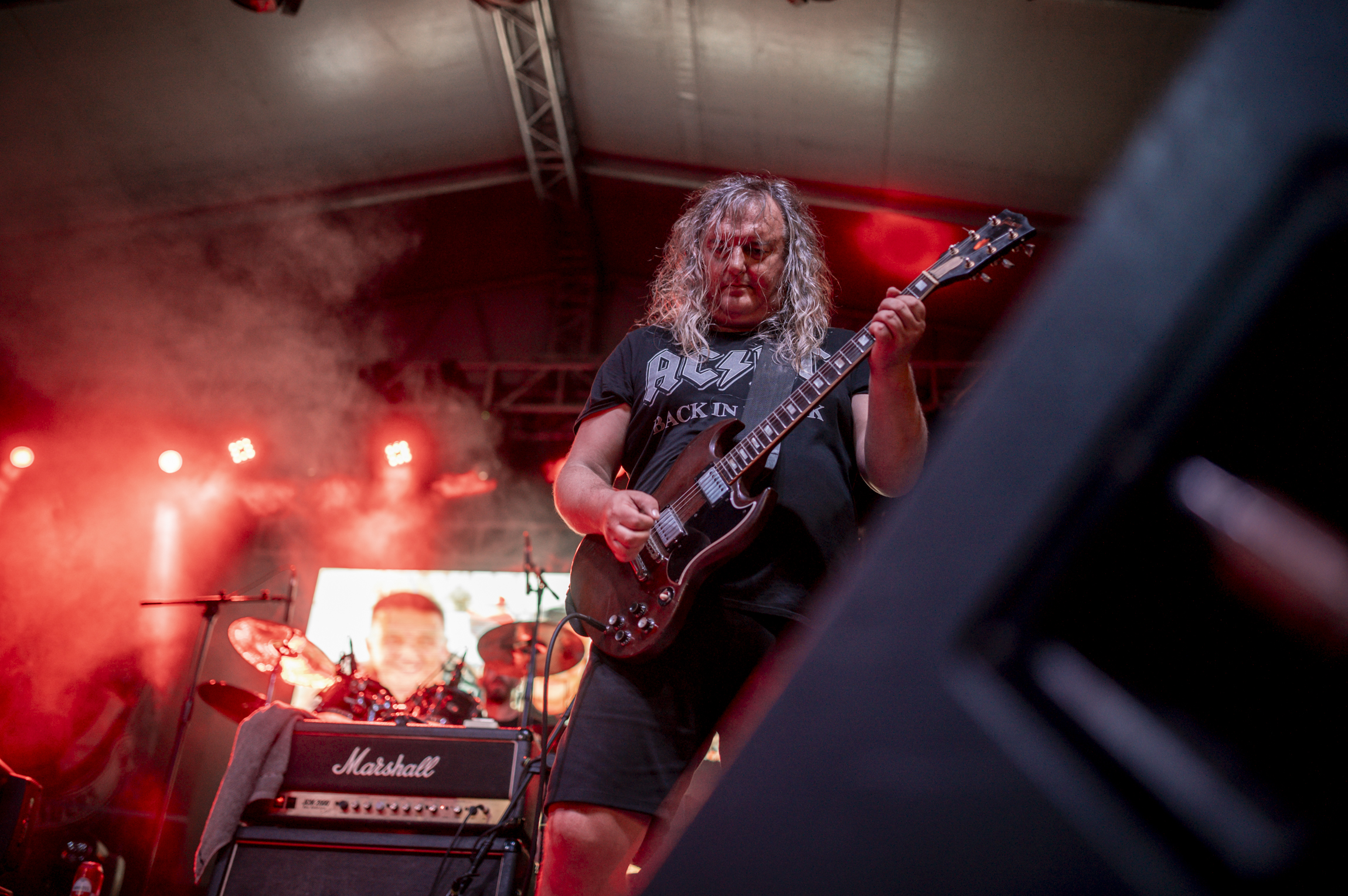 A rock band performs on a brightly lit stage at an outdoor festival while a large crowd watches