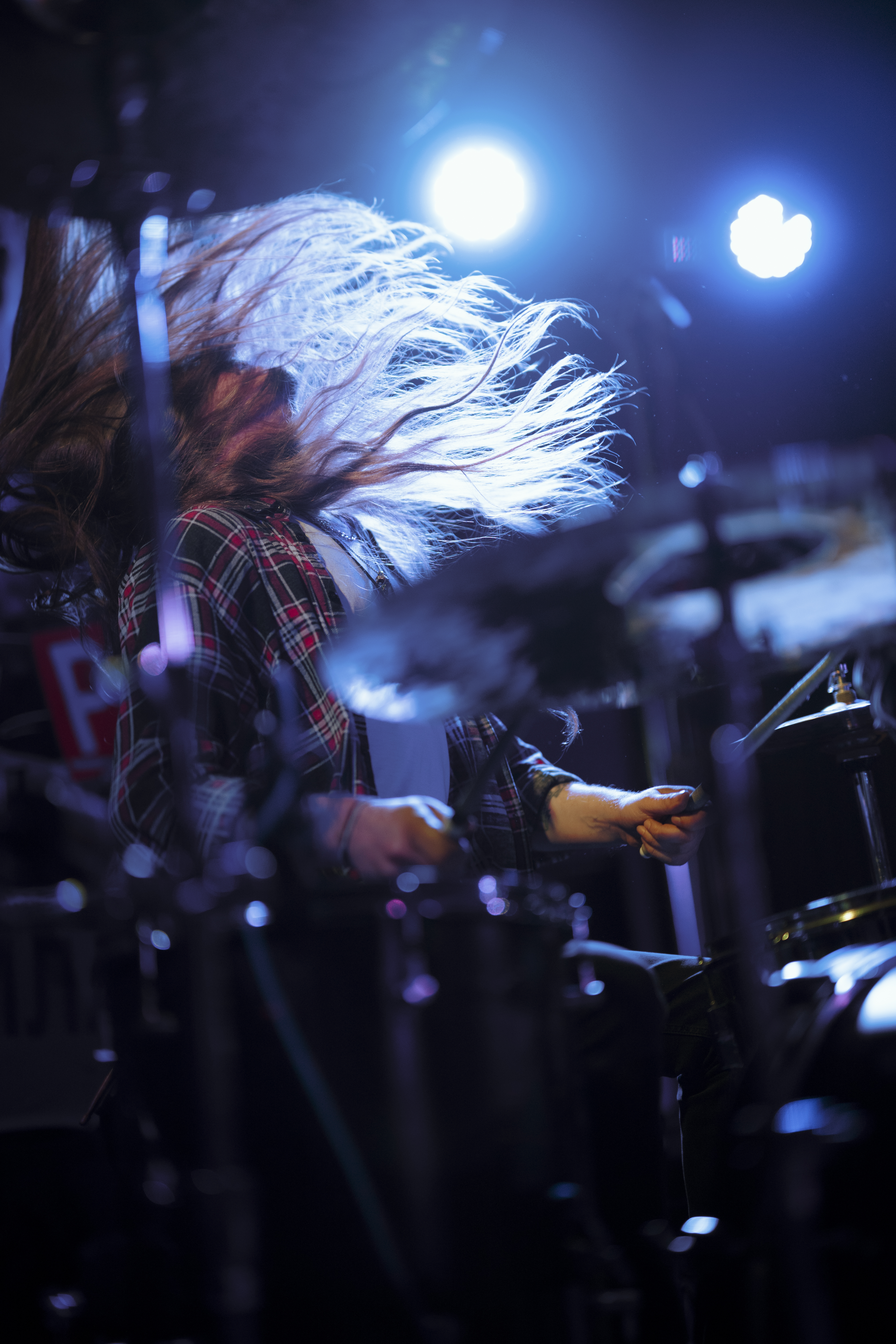 A drummer performs energetically on stage under bright concert lights