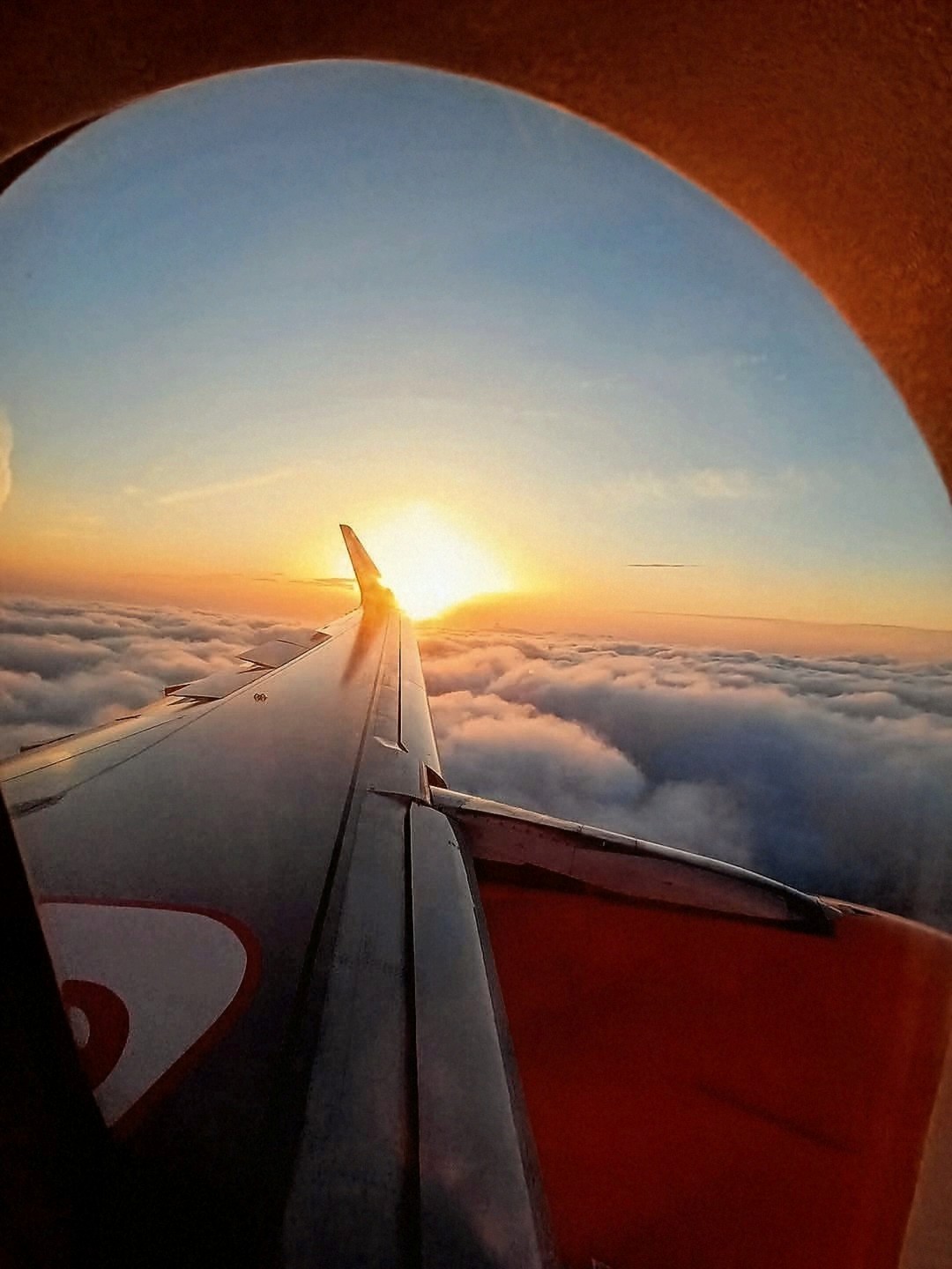 View of an airplane wing from a passenger window above the clouds at sunset