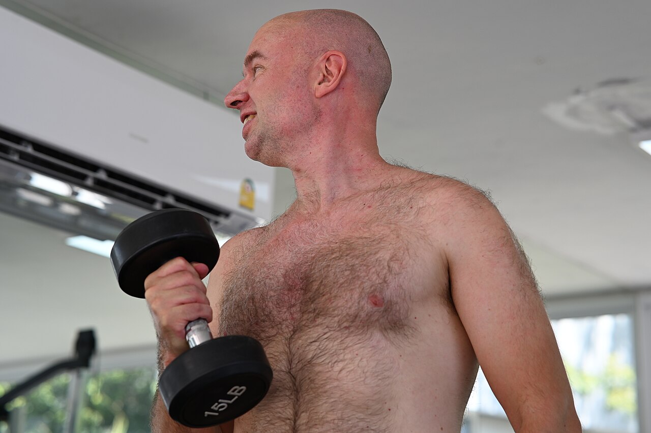 A man training with a dumbbell in a bright gym
