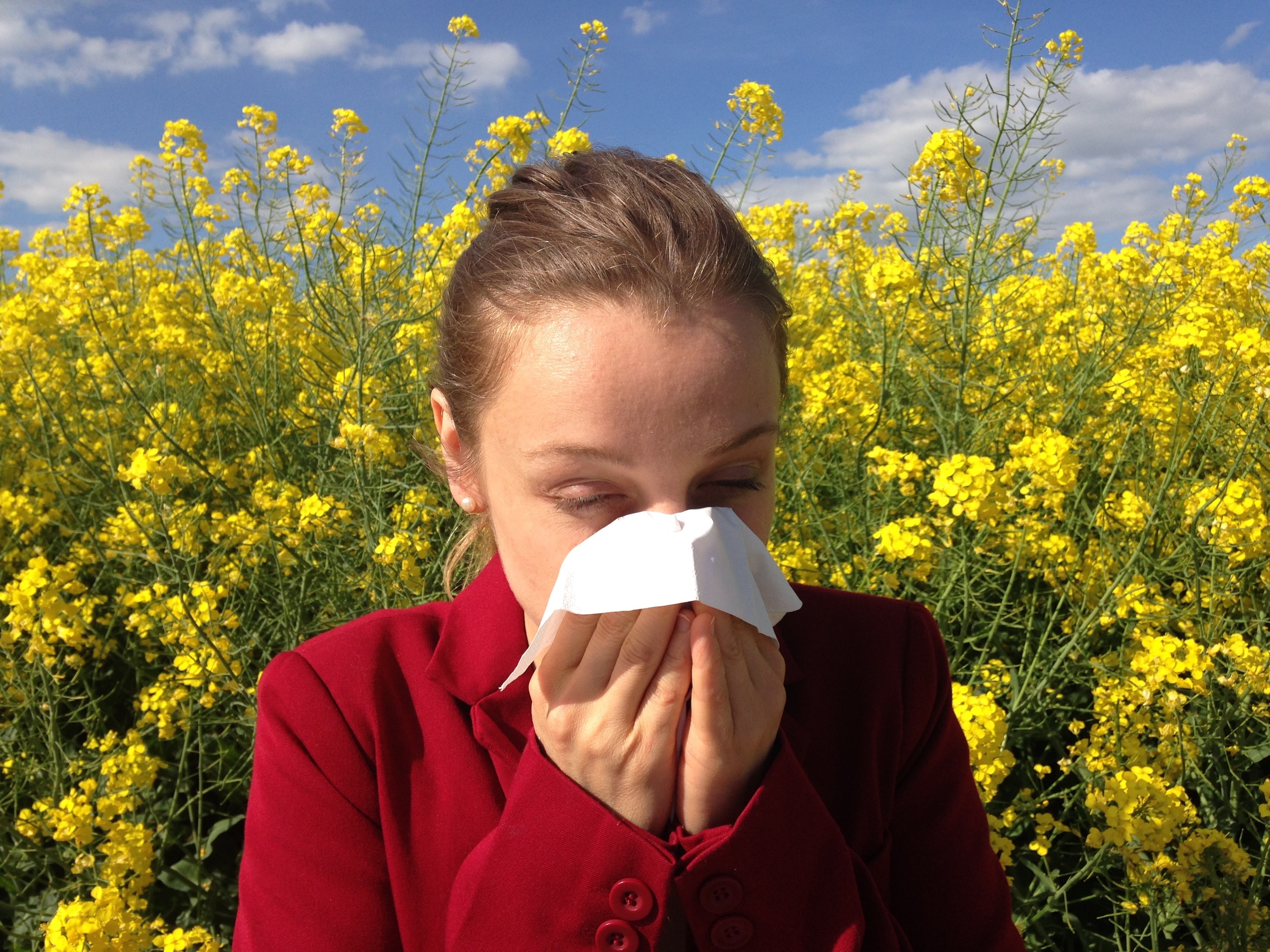 Woman outdoors holding a tissue to her nose in a field of flowers