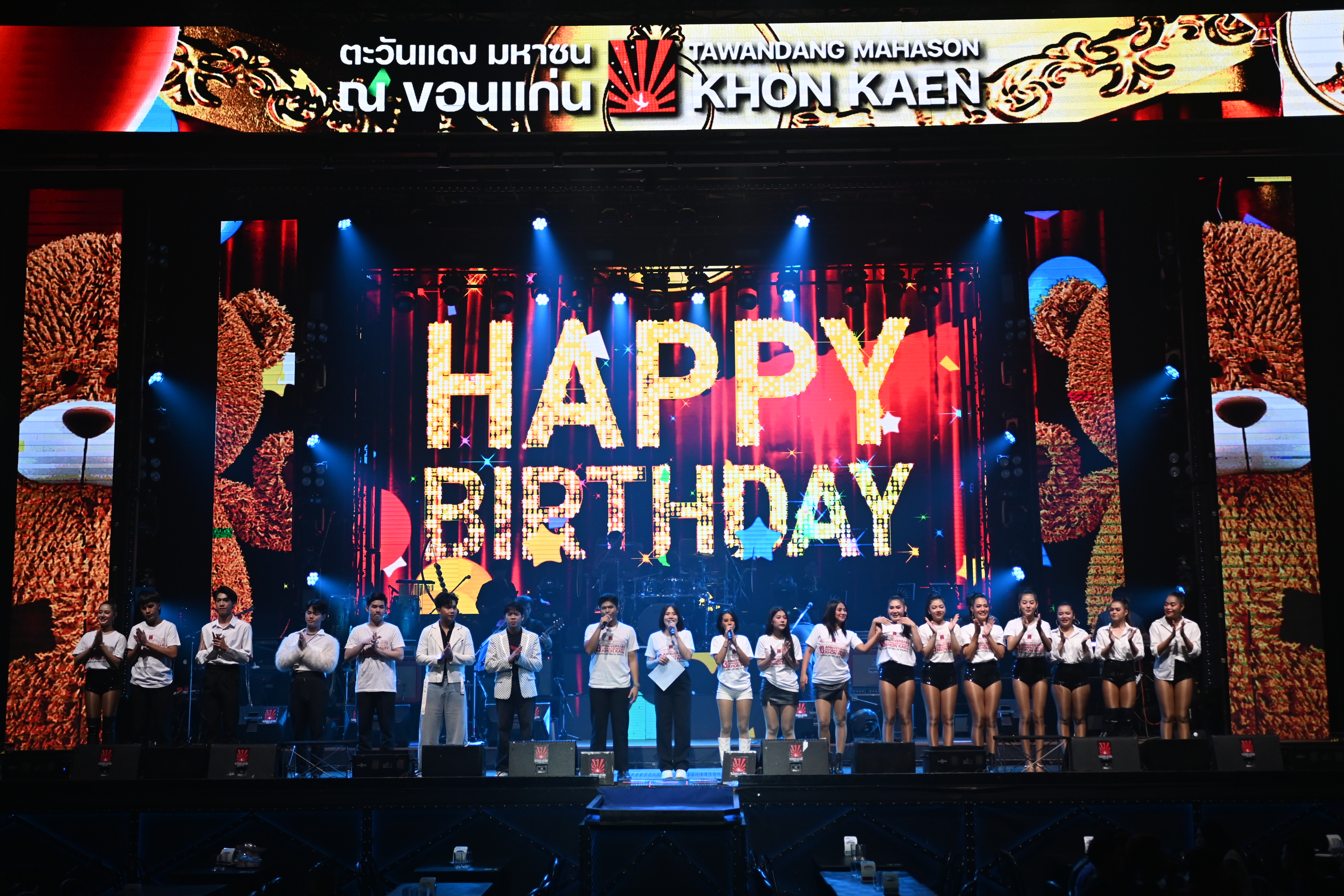 Performers on a brightly lit stage with illuminated lettering