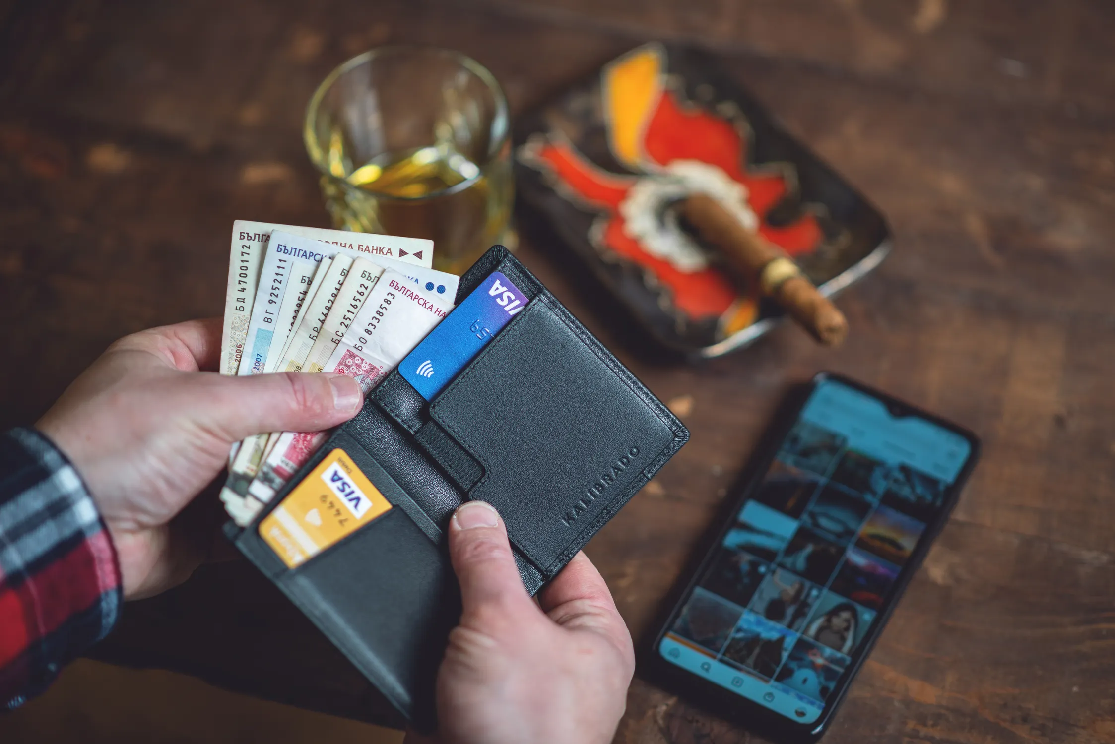 A hand holding a wallet with banknotes and two Visa cards