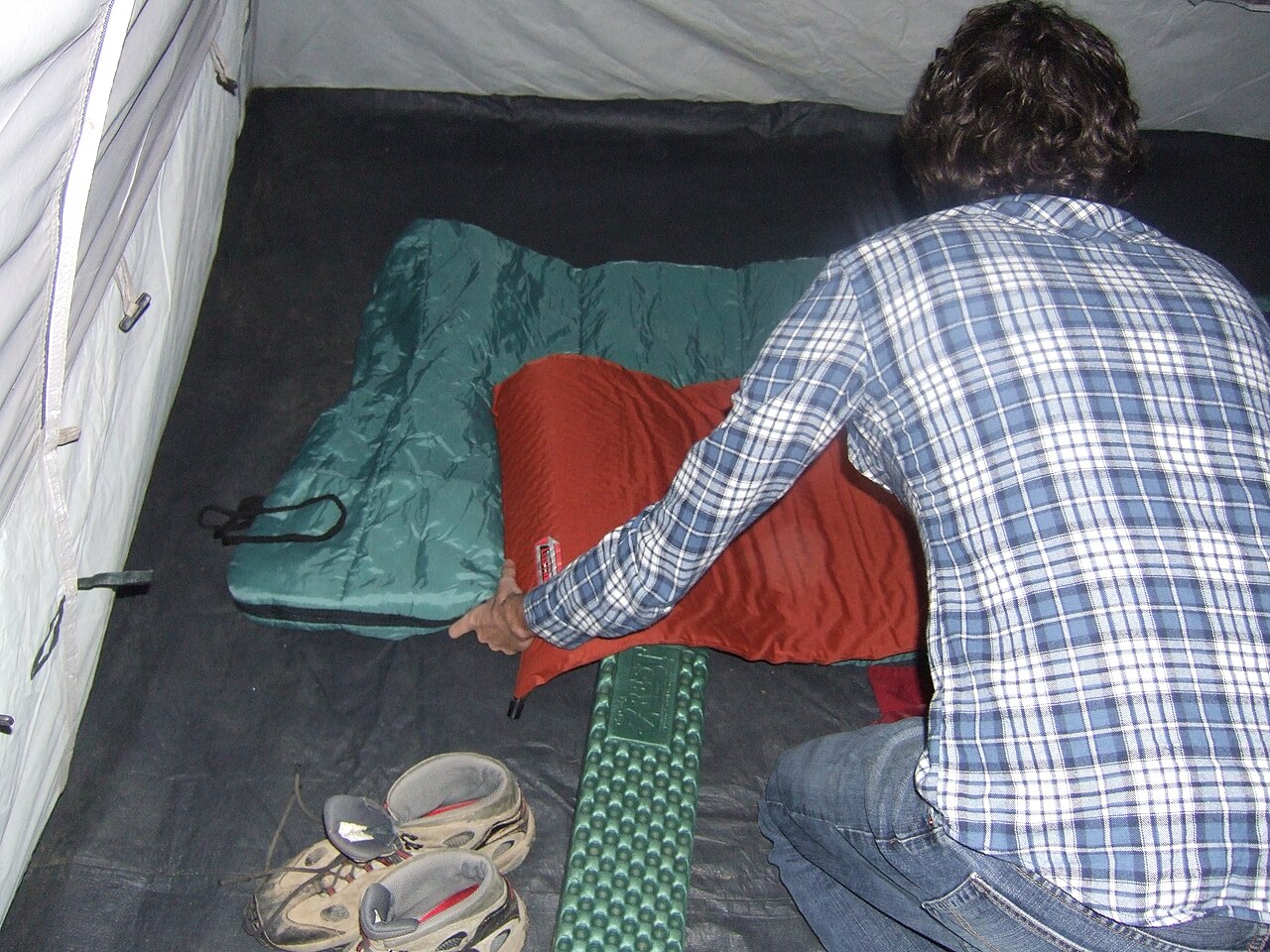 A person adjusting a sleeping bag inside a tent at camp