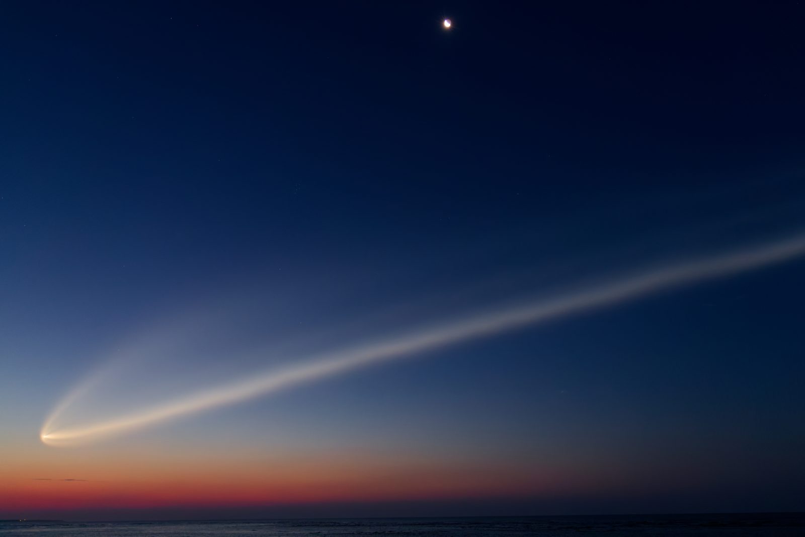 A SpaceX rocket climbs through the sky, leaving a bright trail behind it