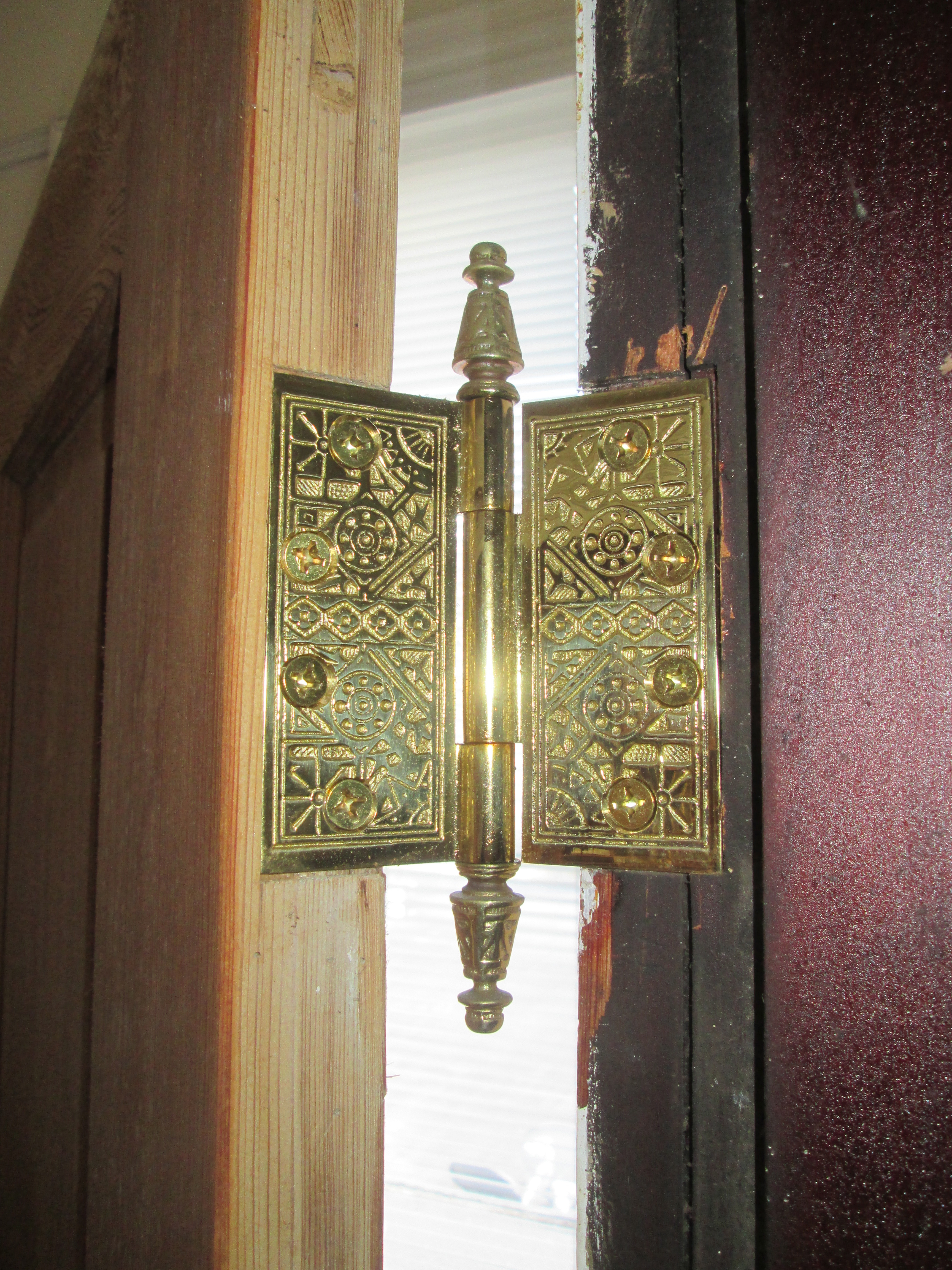 A close-up of an open brass door hinge showing its barrel and mounting screws