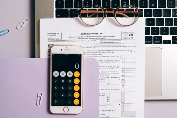 A smartphone calculator app next to a self-employment tax form