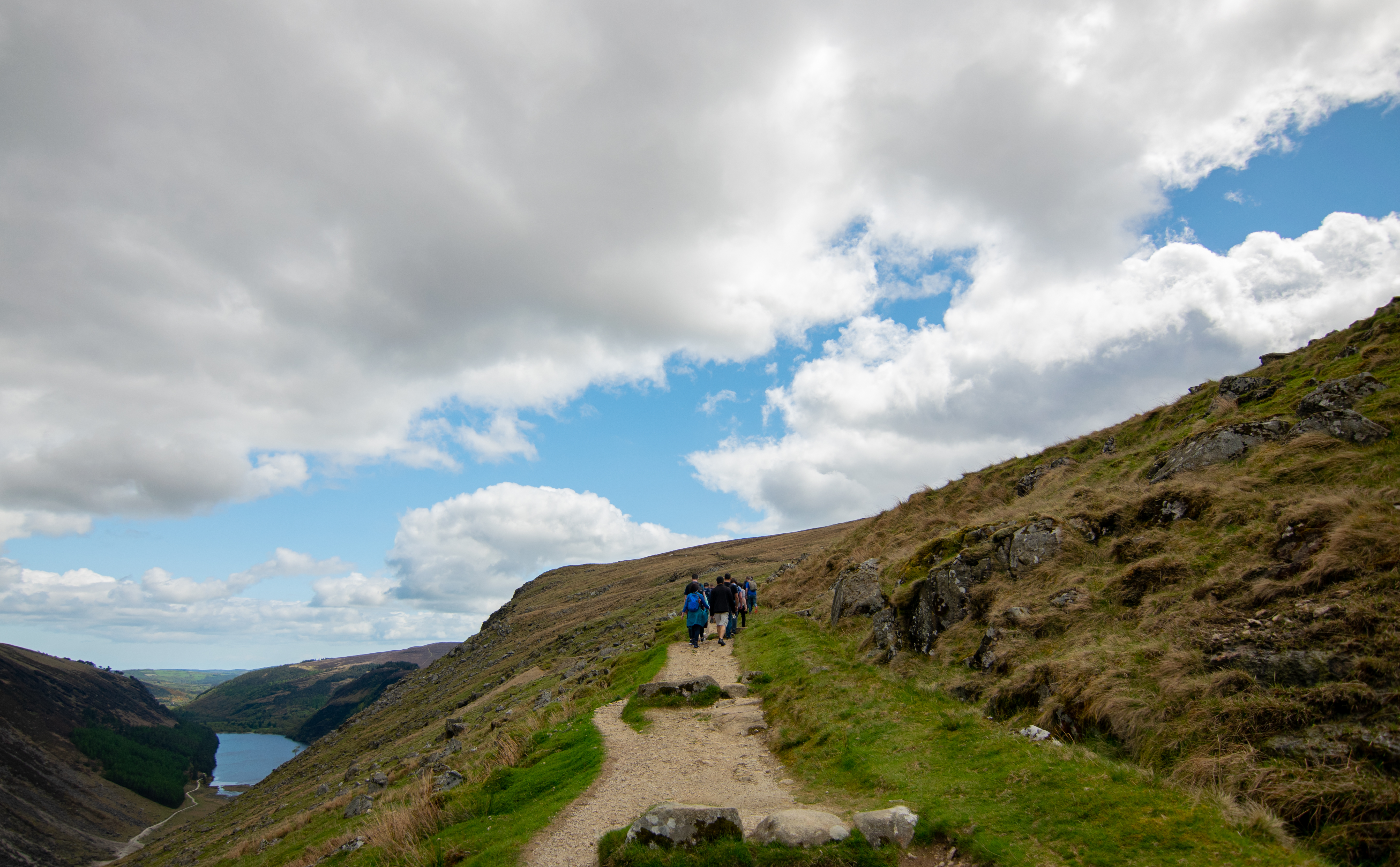 Hikers climbing a steep uphill trail in green hills