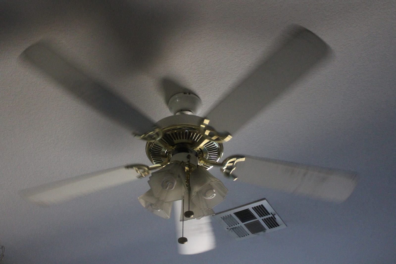 A ceiling fan spinning against a plain ceiling