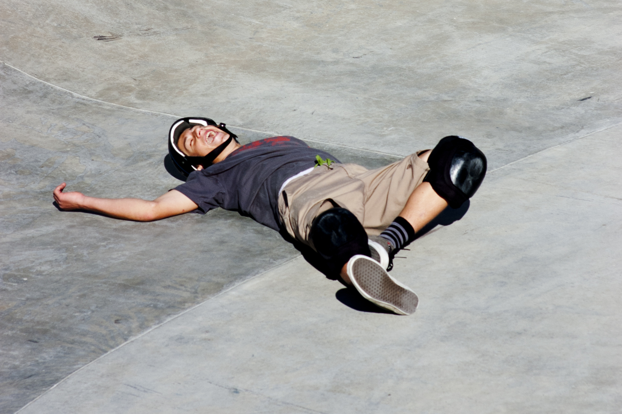 A skateboarder falling sideways at a skatepark, arms tucked in during the fall