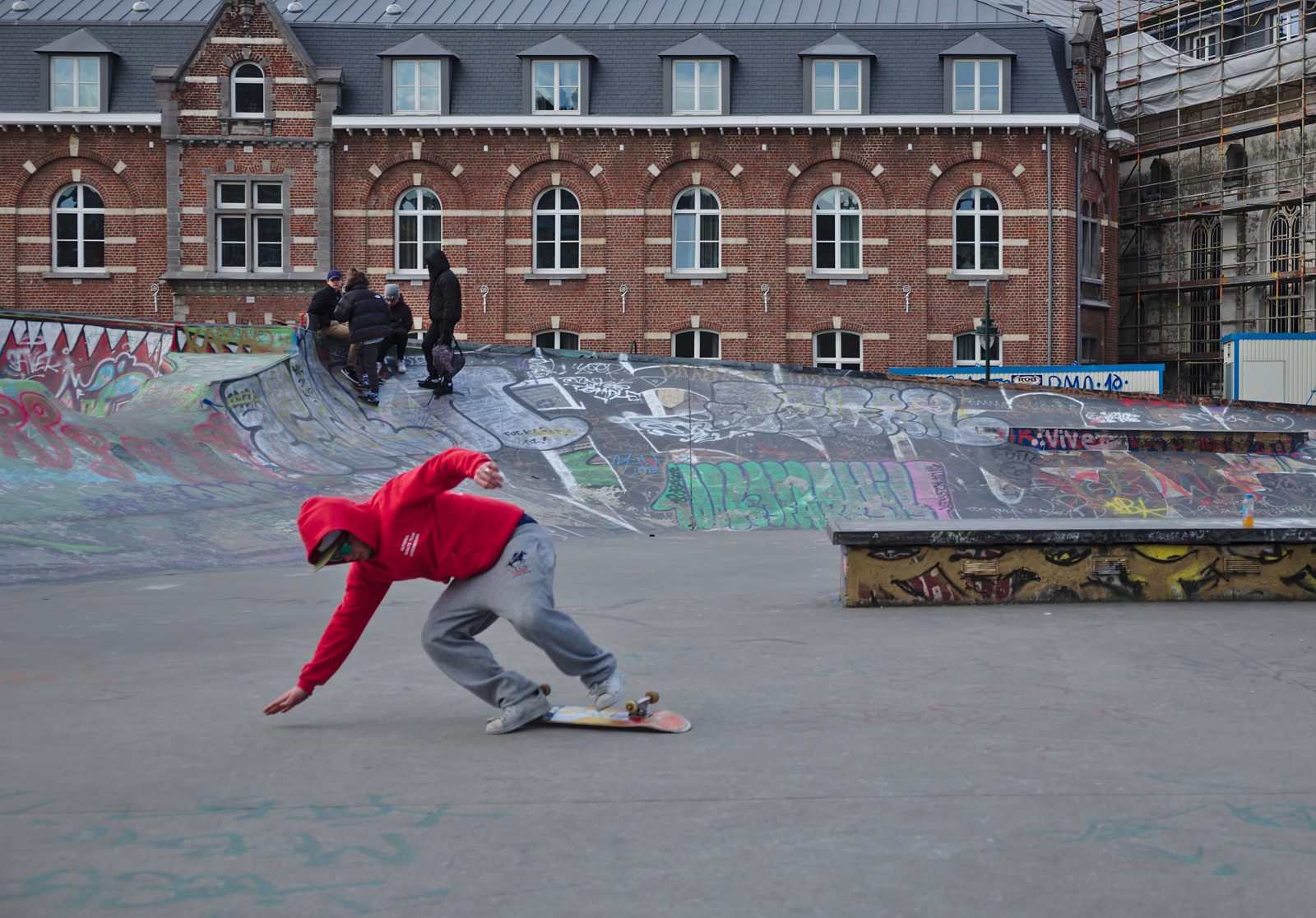 A skateboarder landing low at a skatepark in Brussels, knees bent to absorb the impact