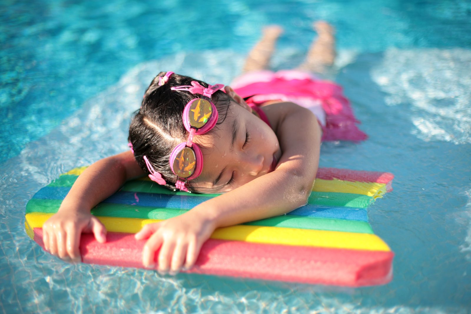 A swimmer with a kickboard at a pool, wearing goggles and a swim cap