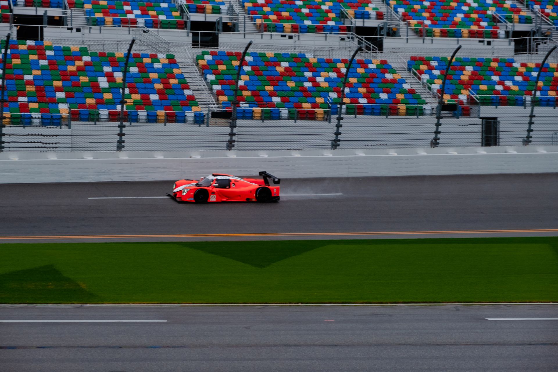 A red race car speeds past colorful seats on a race track during the day