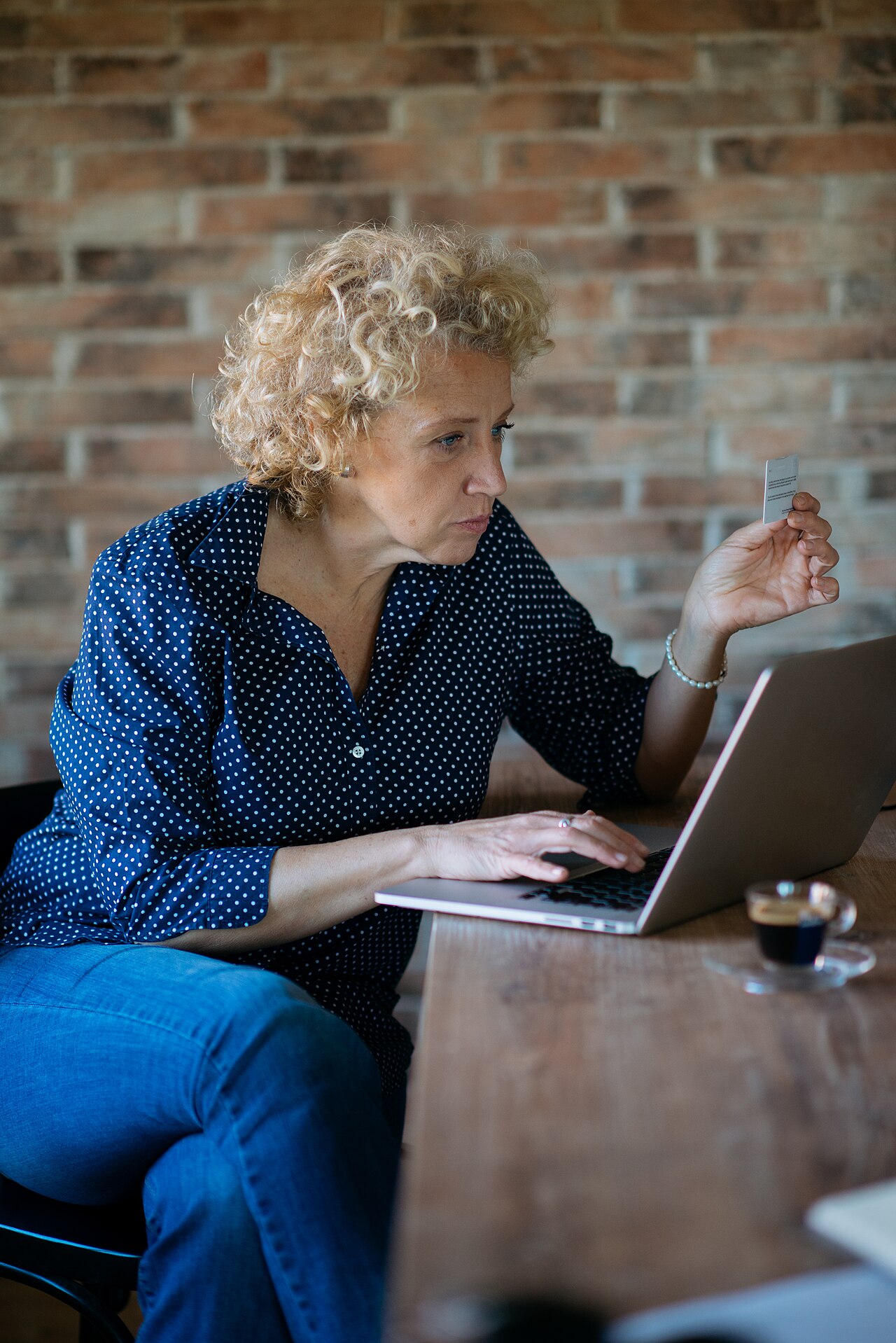 A woman reading from a card while working on a laptop