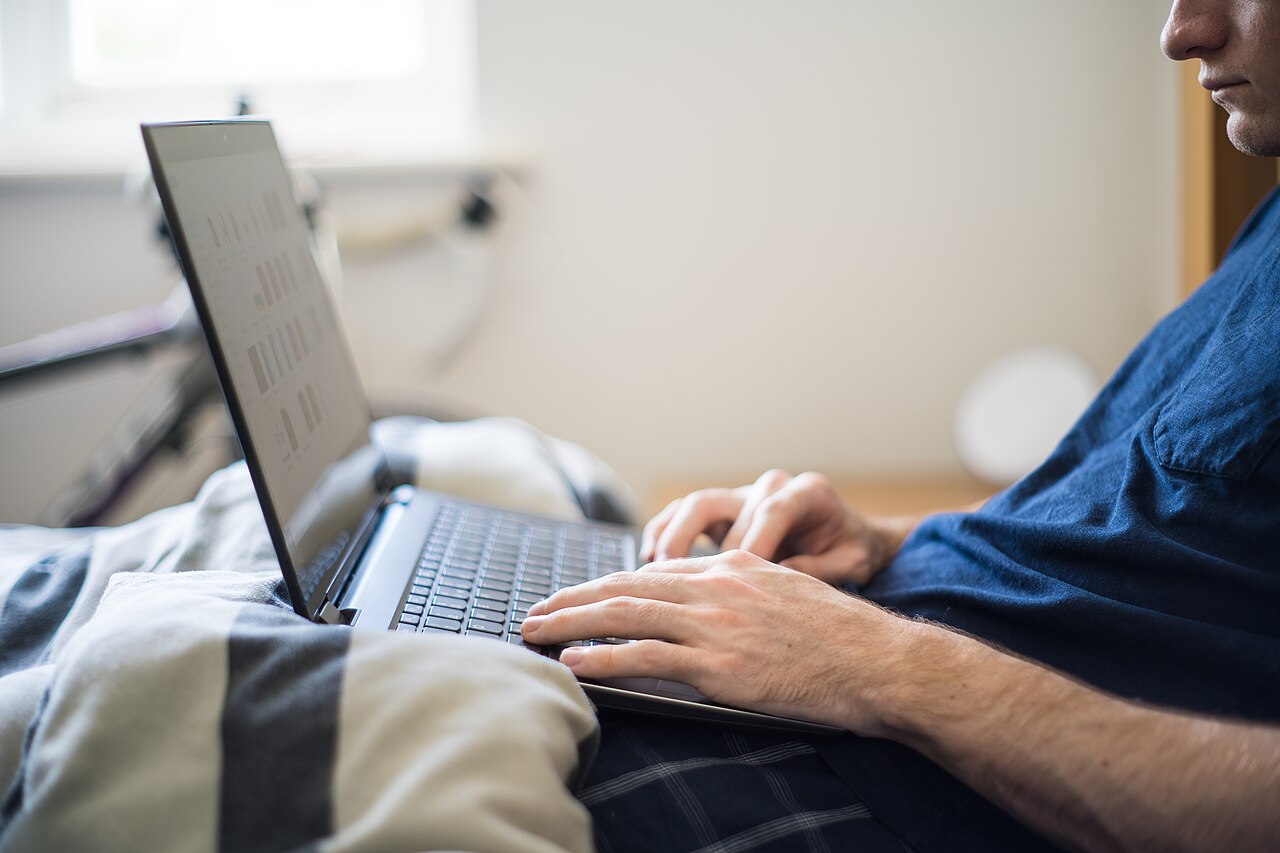 A man working from home with a laptop in bed