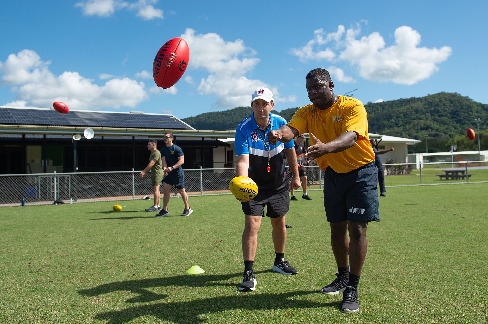 Players learn Australian rules football on an oval field