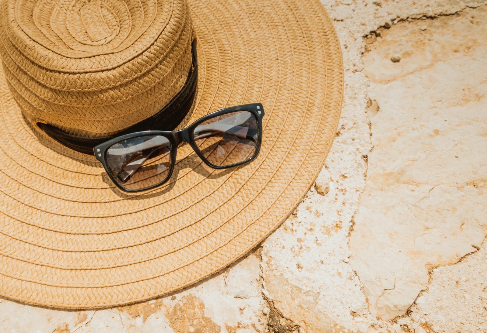 A straw hat and sunglasses resting on a sandy beach